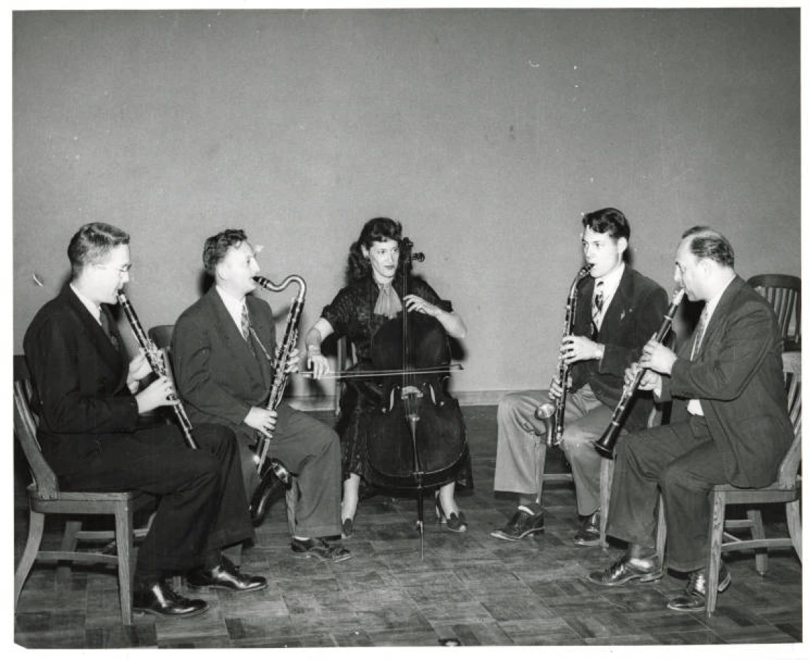 A black and white images of five musicians playing their instruments in a semi-circle.